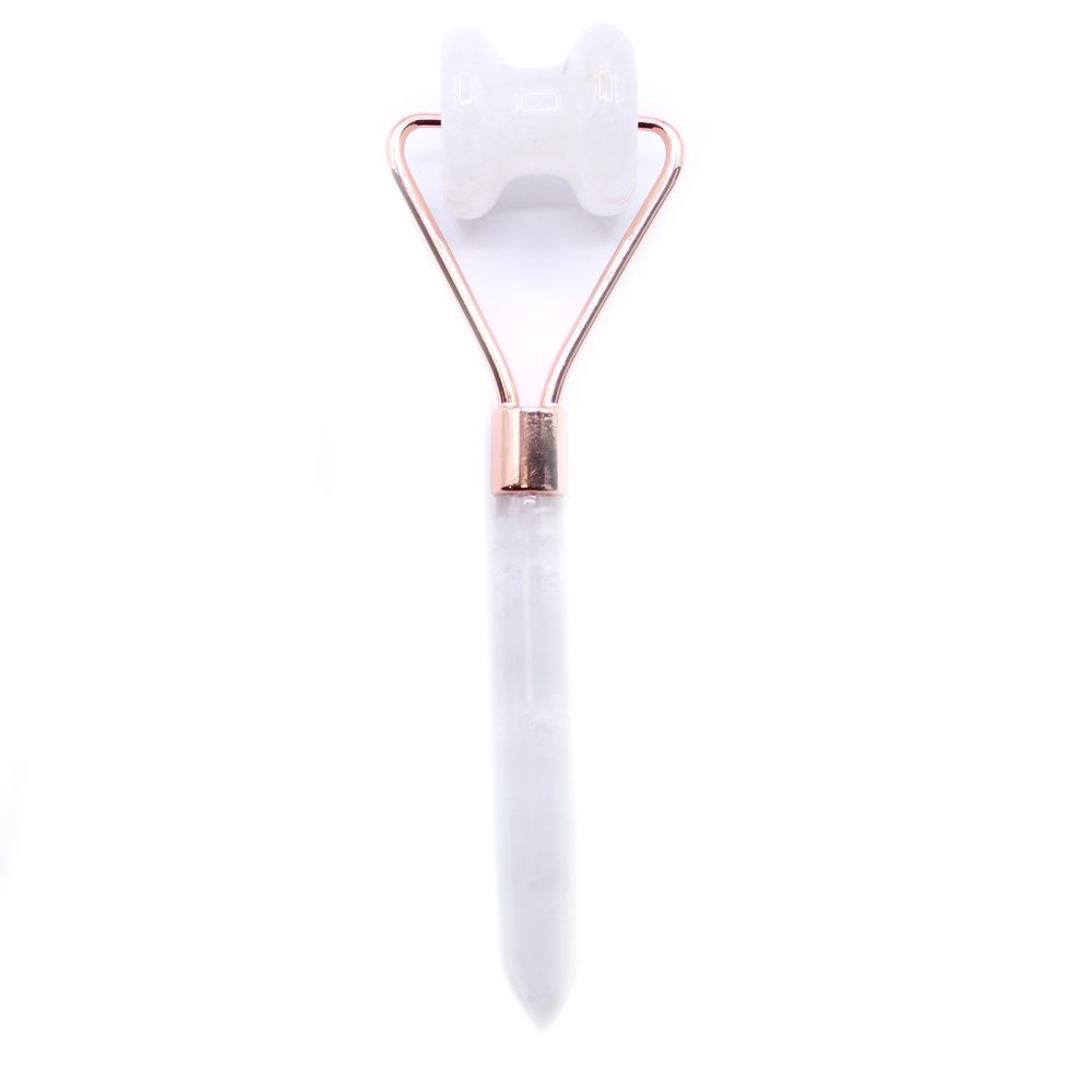 A crystal facial roller sits on a white surface. The roller is made of white quartz and has a copper-colored handle.