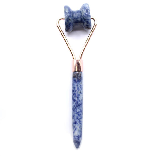 A blue sodalite facial roller stands upright. It features a handle and a rolling head on a gold-colored frame, and it is set against a white background.