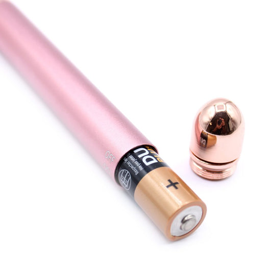 A pink electric device accepts a "DU Respecter les Ne Pas jeter" AA battery; the device's rose-gold cap lies nearby. It is on a white surface.