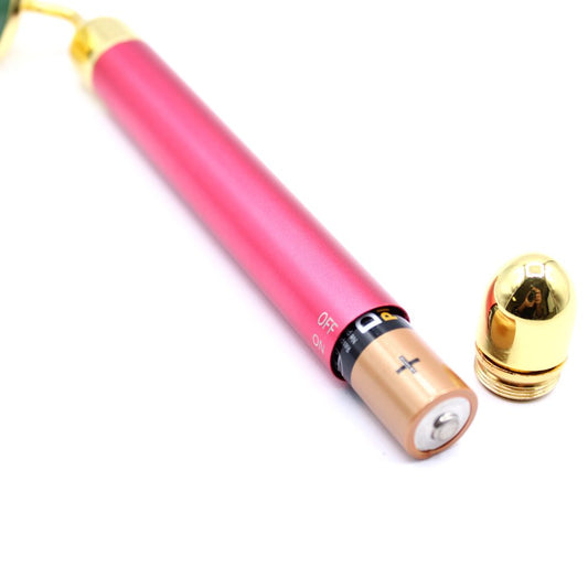 A pink cylindrical device has its battery exposed. The “OFF” and “ON” labels are next to the battery slot. A gold cap sits nearby on a white surface.
