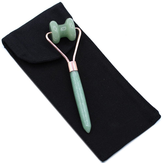 A green facial roller rests diagonally on a black cloth bag. The roller's handle is a smooth cylinder, and the rolling part is shaped like two squat barrels.