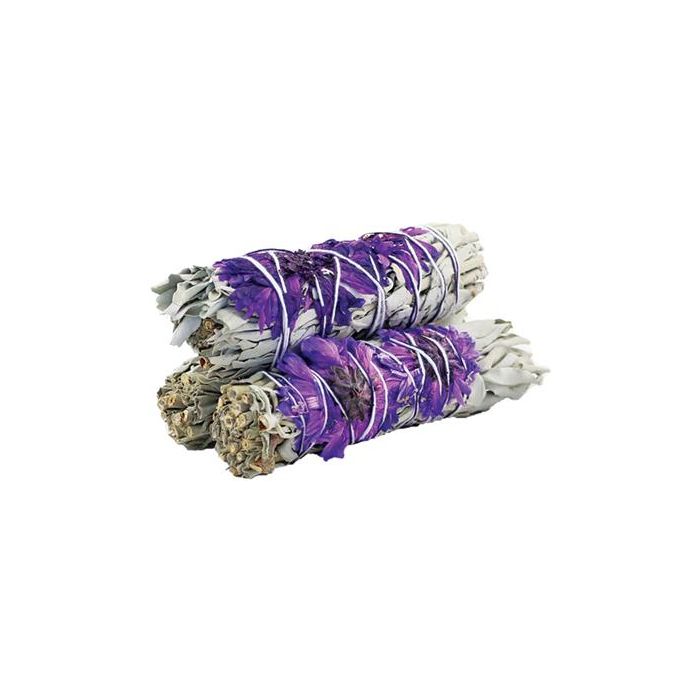 Three sage bundles, tied with string and decorated with purple flowers, sit stacked on a plain white surface.