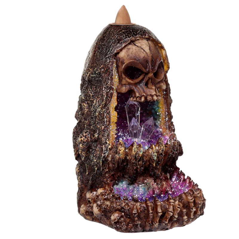 A decorative incense holder with a skull design and crystal interior, cascading smoky colors. It sits in a grotto-like structure, combining rustic and mystical elements.