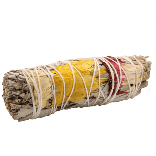 A sage smudge stick wrapped with white string is adorned with yellow and red flower petals against a dark green background.