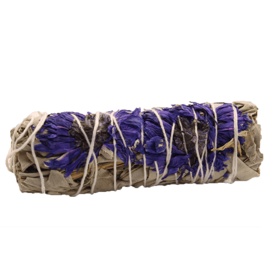 A smudge stick rests on a solid green surface, its dried sage and blue petals bound together with white string.