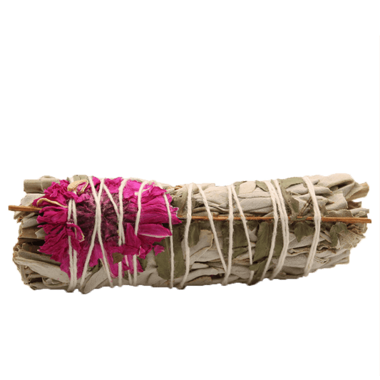 A sage bundle, tied with string, features a pink flower embedded on one end. The bundle lies horizontally in the center against a solid green background.