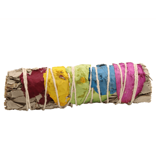 Bundled sage and colorful flower petals are secured with white string, forming a log shape, set against a solid green background.