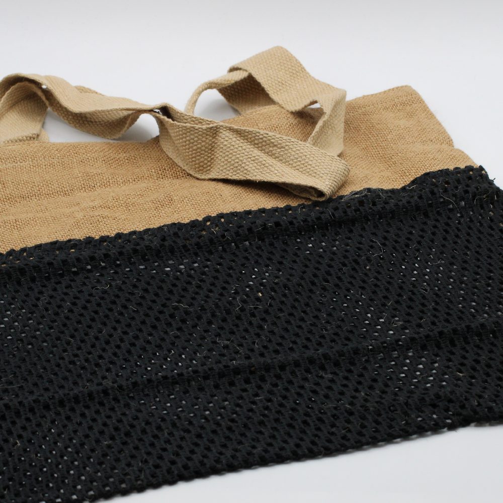 A tan jute tote bag, with woven handles, features a wide band of black netting. It rests on a white surface.