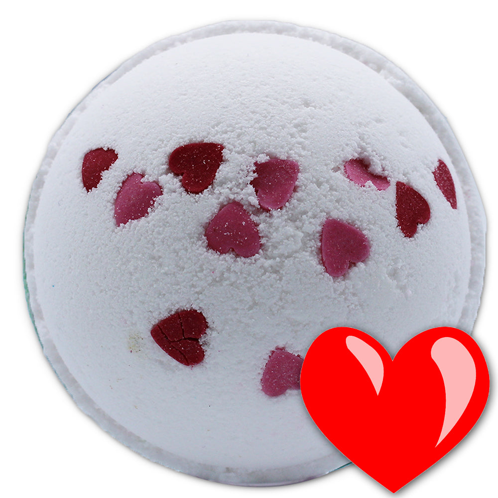 A round, white bath bomb with embedded red and pink heart shapes, placed on a plain background. A large, red heart symbol overlaps the bottom right corner.