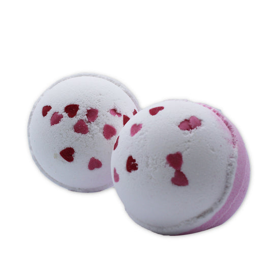Two white and pink bath bombs, adorned with scattered pink and red heart-shaped patterns, rest on a white surface.