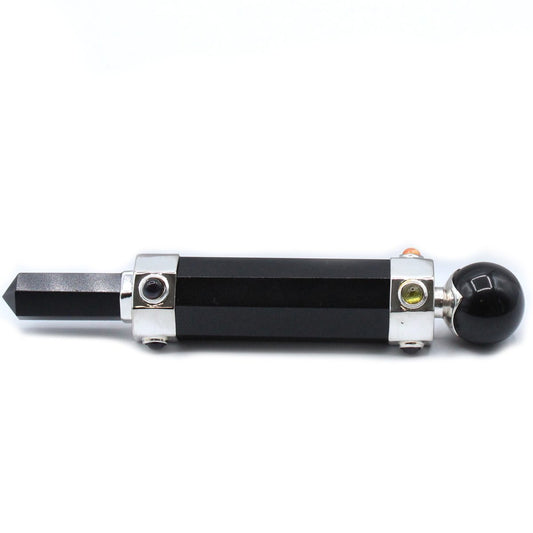 A black, cylindrical wand with a pointed tip and a ball end lies horizontally, accented with silver bands and small gemstones against a white background.