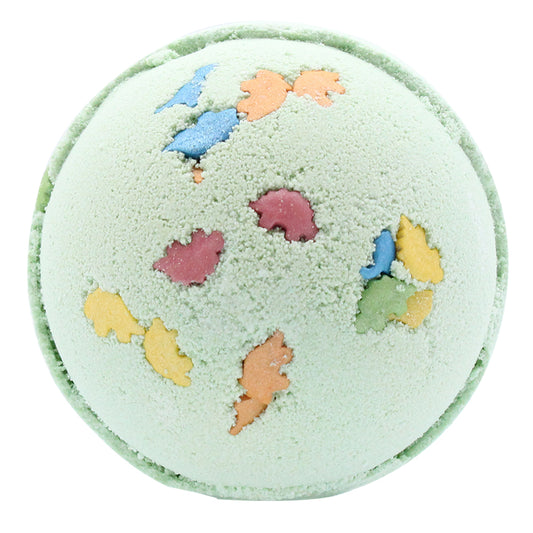 A round, light green bath bomb features colorful dinosaur-shaped imprints, including blue, orange, and pink silhouettes, against a plain white background.