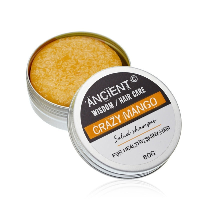 A round, solid, mango-scented shampoo bar sits in an open, silver, tin container. The lid displays the text: "ANCIENT WISDOM / HAIR CARE CRAZY MANGO Solid shampoo FOR HEALTHY, SHINY HAIR 60G".