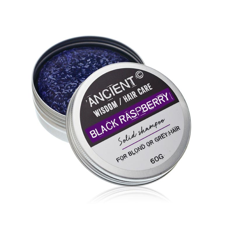 A black solid shampoo bar sits inside an open silver tin. Next to it is the lid of the tin, which reads: "ANCIENT WISDOM / HAIR CARE BLACK RASPBERRY Solid shampoo FOR BLOND OR GREY HAIR 60G."