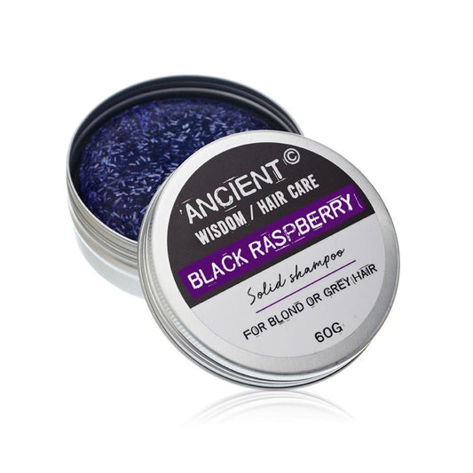 A metal tin of purple shredded solid shampoo sits with its lid tilted to show the label reading ANCIENT © WISDOM / HAIR CARE BLACK RASPBERRY Solid shampoo FOR BLOND OR GREY HAIR 60G. on a white background