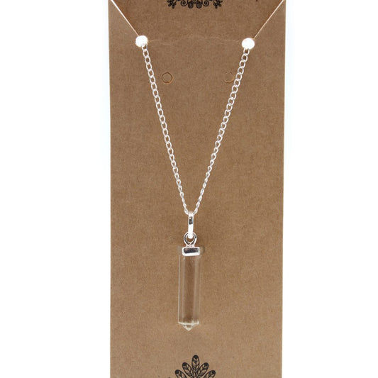 A clear, crystal pendant hangs from a delicate silver chain on a display card. The card is brown and has ornate designs on the top and bottom.