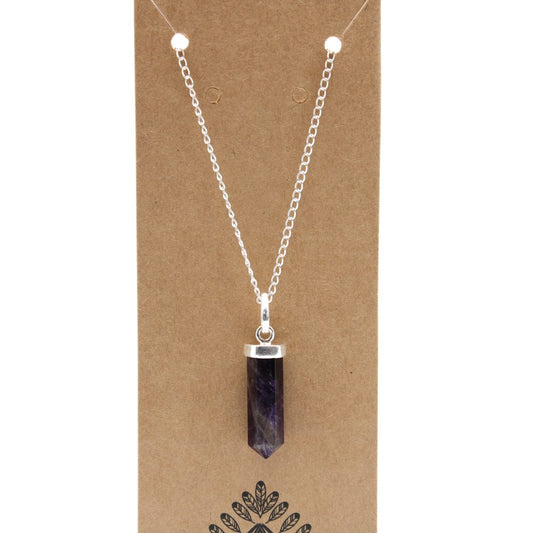 A silver chain necklace with a purple, pointed pendant hangs against a tan cardboard display, secured by small silver circles.