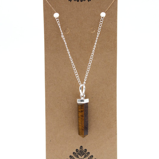 A tiger's eye crystal necklace with a silver chain hangs against a brown cardboard backing. The pendant is a slim, pointed hexagon.