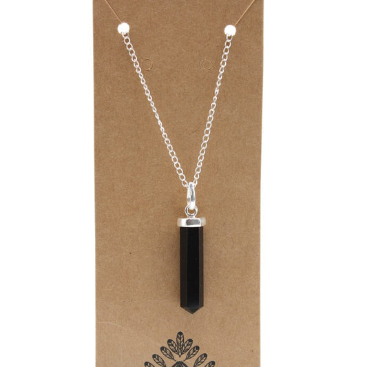 A black, crystal-shaped pendant hangs from a silver chain. It is displayed against a plain, brown cardboard backing with a leafy design printed at the bottom.