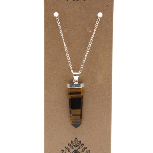 A tiger-eye pendant hangs from a silver chain against a brown cardboard display. The stone is shaped like a tapered prism with dark bands.