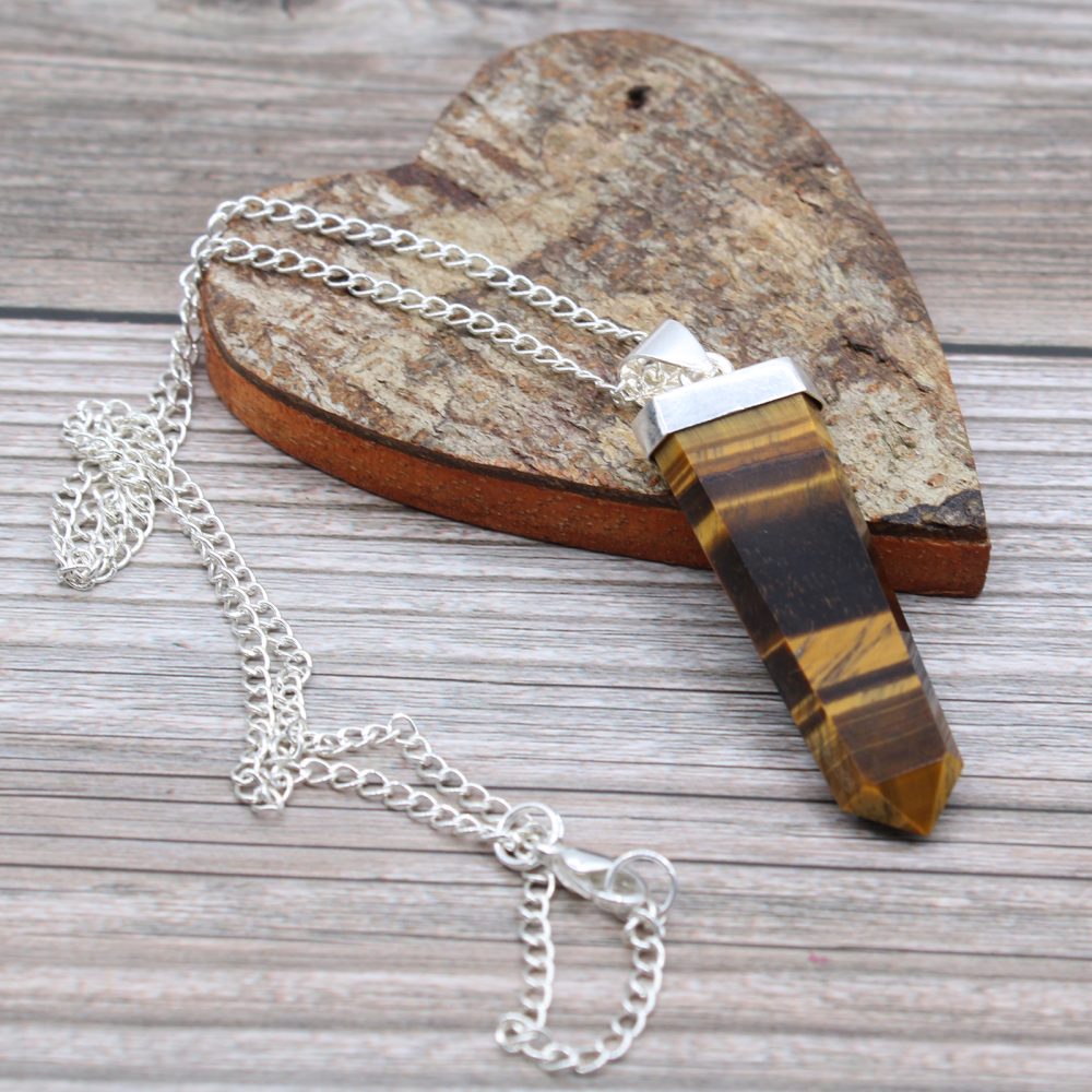 A tiger's eye crystal pendant with silver findings and chain lies on a wooden heart, which sits on a rustic wooden surface.