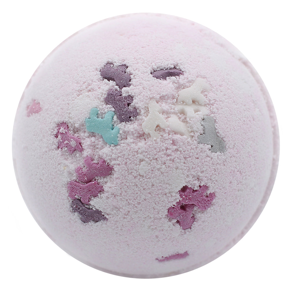 A pastel pink bath bomb is adorned with colorful, shaped sprinkles, featuring small animal figures. It's set against a simple white background, highlighting its textured surface.