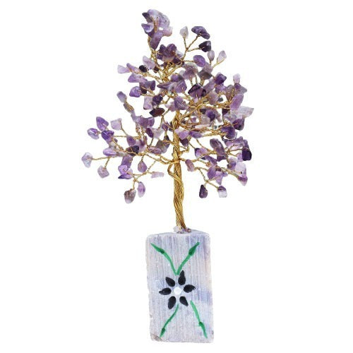 A small, decorative tree stands, constructed from gold wire with small, purple gemstone "leaves," anchored in a pale blue and white stone vase adorned with a black flower.