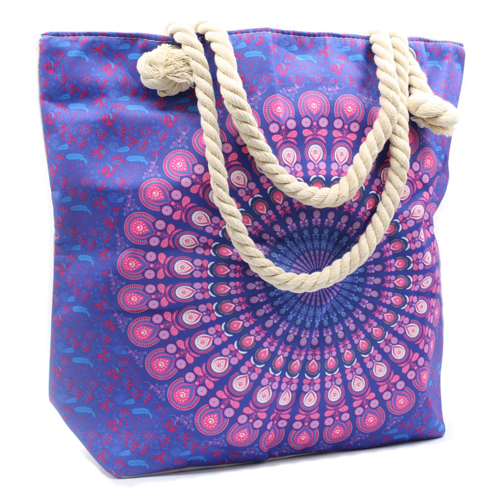 A large blue tote bag, patterned with a pink and purple mandala design, has rope handles. The bag sits upright against a white background.