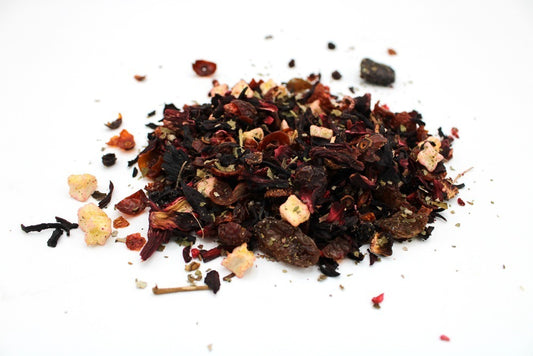 A loose pile of dried fruit tea blend with hibiscus, rose hips, apple pieces, and other botanical ingredients rests on a white surface.