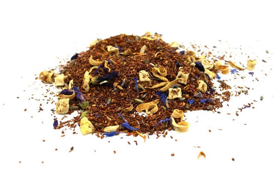 A pile of loose leaf tea blend, featuring rooibos, dried fruit pieces, and blue petals, rests on a white background, showcasing a colorful and textured assortment.