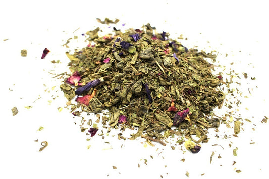 A pile of mixed tea leaves with colorful flower petals, including pink and purple, rests on a white surface, scattered slightly around the edges.
