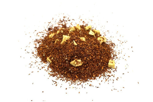 A pile of loose rooibos tea mixed with small chunks of dried fruit sitting on a white background, showcasing a rich, reddish-brown color.