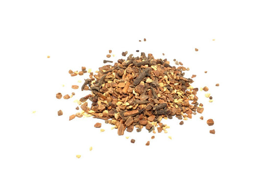 A pile of mixed spices, including cloves and crushed cinnamon, sits scattered on a white surface, creating a visually textured, aromatic display.