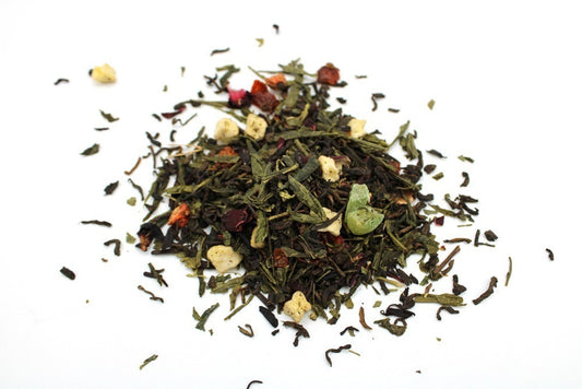 A small pile of loose-leaf tea mix, containing green and dark leaves, along with small pieces of dried fruit, rests on a white surface.