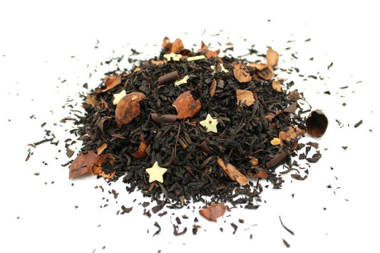 A pile of loose tea leaves mixed with small chocolate curls and star-shaped sugar pieces, scattered against a plain white background.