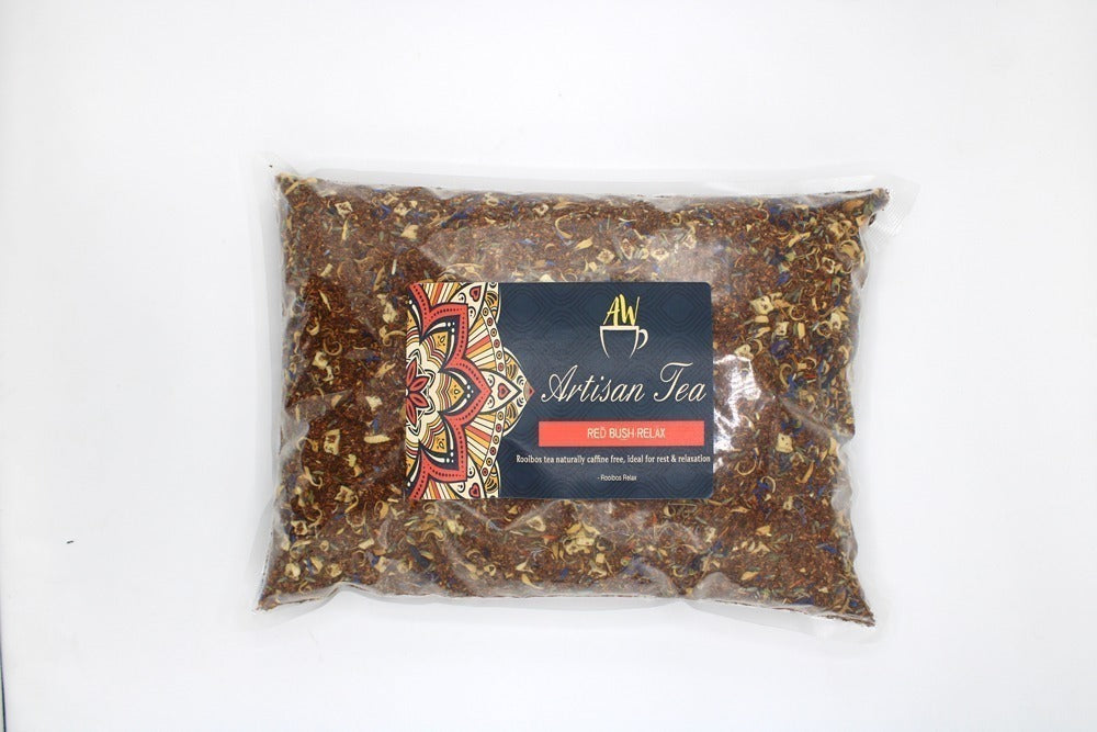 A plastic bag filled with loose tea labeled "AW Artisan Tea," featuring a colorful mandala design. Text reads: "RED BUSH RELAX. Rooibos tea naturally caffeine free. Ideal for rest & relaxation." The bag rests on a white surface.