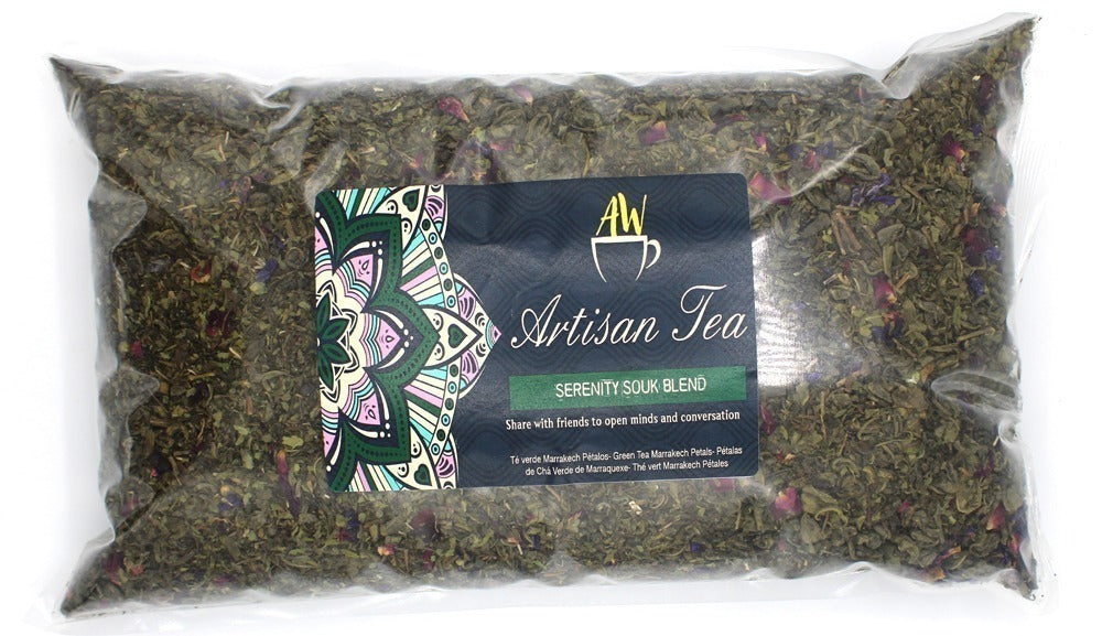 A clear plastic bag contains loose green tea leaves with colorful petals. The label reads, "AW Artisan Tea, SERENITY SOUK BLEND. Share with friends to open minds and conversation." Decorated with a floral pattern.