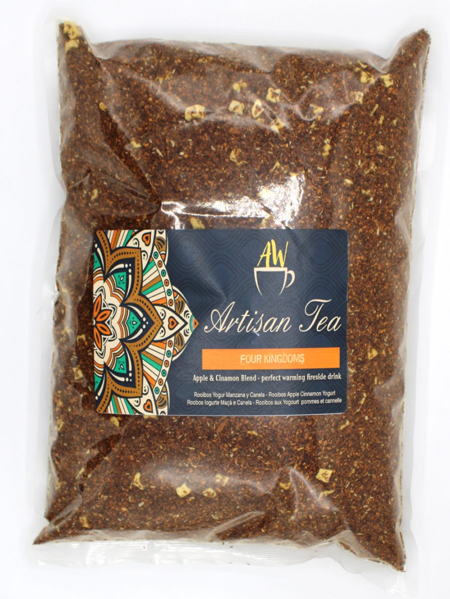 A clear plastic bag contains loose rooibos tea with apple and cinnamon pieces. The label reads: "AW Artisan Tea, FOUR KINGDOMS, Apple & Cinnamon Blend – perfect warming fireside drink." Colorful mandala design.