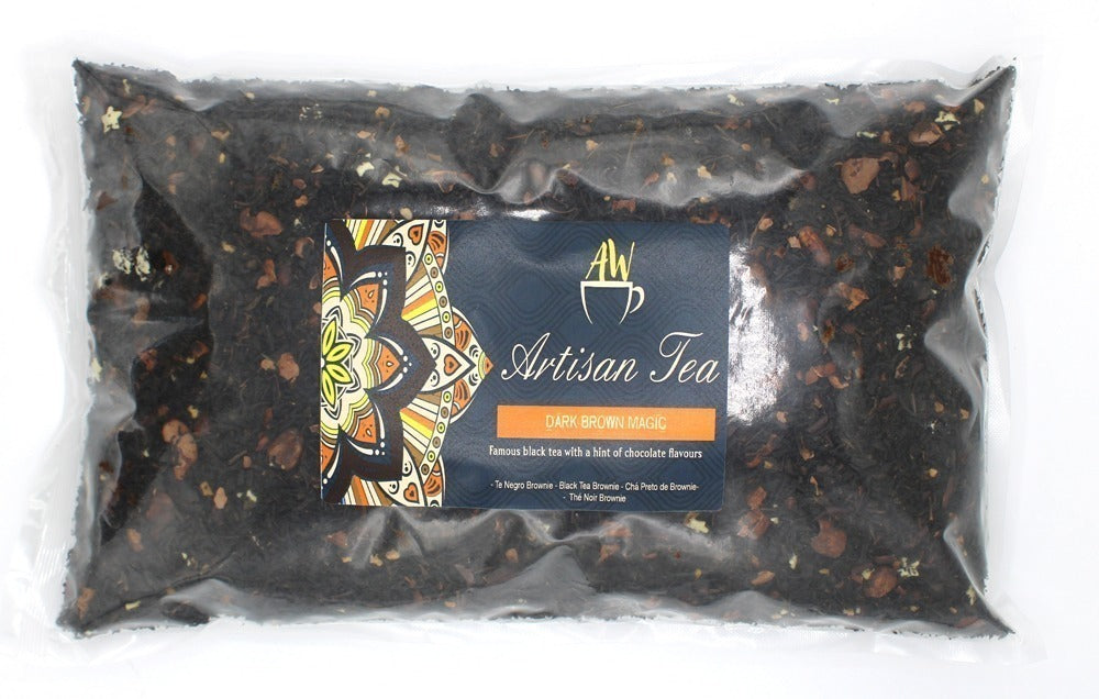 A sealed plastic bag contains loose black tea leaves with scattered light brown pieces. A label reads: "AW Artisan Tea, DARK BROWN MAGIC, Famous black tea with a hint of chocolate flavours," and is decorated with a colorful mandala.