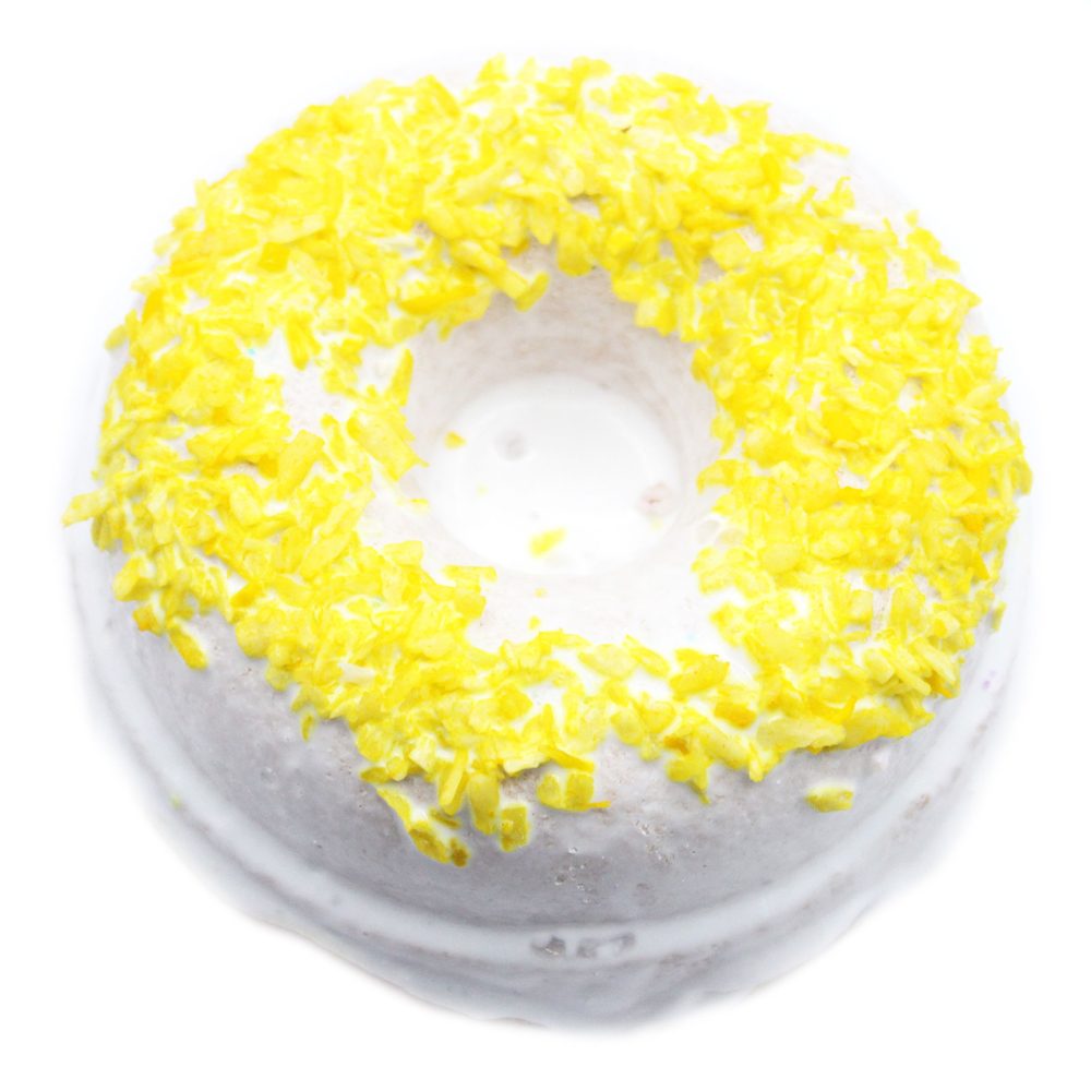 A round white bath bomb is topped with vibrant yellow flakes, evoking a refreshing citrus theme. It rests against a plain white background, highlighting its vivid color contrast.