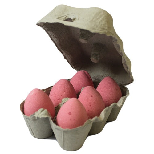 Pink eggs sit in an open cardboard carton, which holds six eggs in a neutral, grayish tone, creating a unique visual contrast.