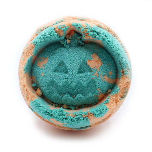 A round, turquoise bath bomb features a carved pumpkin face, with orange patches, appears crumbly on a white background.