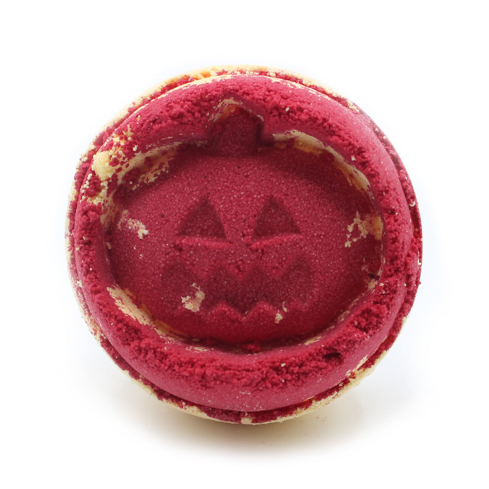 Red, round cookie with a carved pumpkin face design is placed against a plain white background. Crumbs and light texture detail the surface, enhancing its Halloween theme.