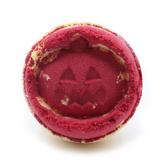 Red, round cookie with a carved pumpkin face design is placed against a plain white background. Crumbs and light texture detail the surface, enhancing its Halloween theme.