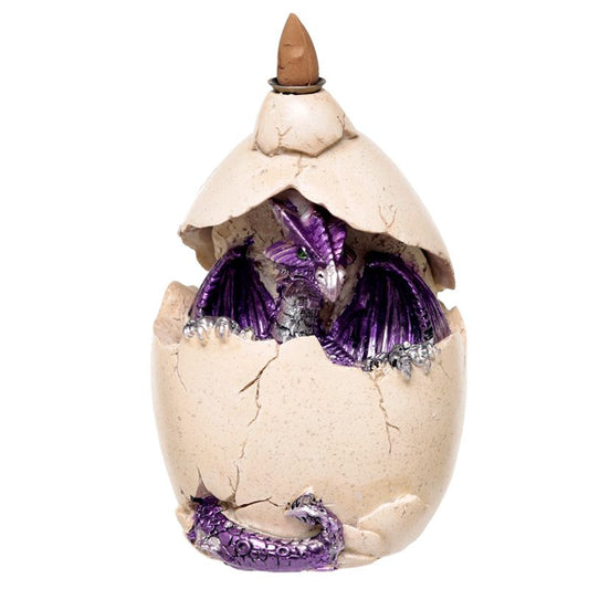 A purple dragon figurine emerges from a cracked eggshell, with detailed scales and wings, partially concealed inside the broken shell. The environment is plain, showcasing the dragon's vivid colors.