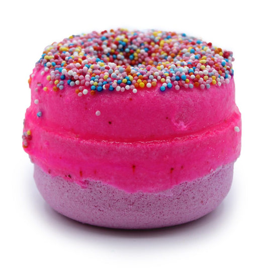 A donut-shaped bath bomb, with pink frosting and colorful sprinkles, rests against a plain white background.
