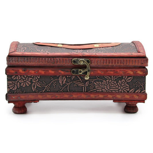 A decorative wooden box, featuring floral carvings, rests on four small feet. It is closed with a brass latch and has a leather handle on top, set against a plain background.