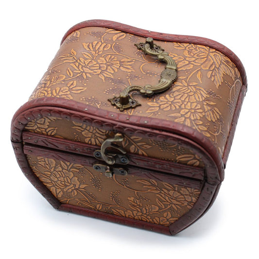 A small, vintage-style chest with intricate floral patterns and a curved metal handle rests on a plain surface, featuring decorative detailing and a prominent latch for closure.