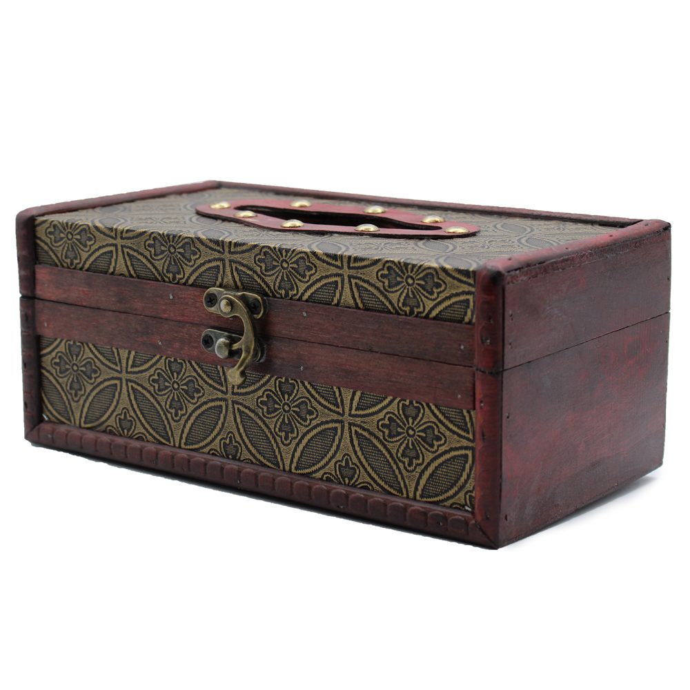 A wooden box with brass hardware sits closed, featuring intricate floral patterns on fabric-covered panels. The box is in a plain, white setting.
