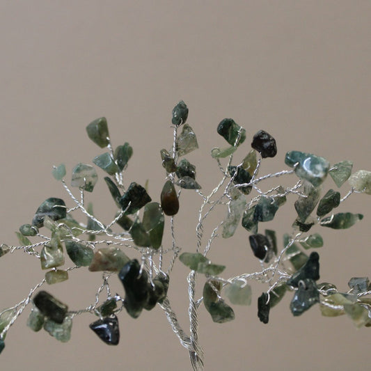 A wire tree displays polished green-and-white stones as leaves, filling the frame against a light tan background.